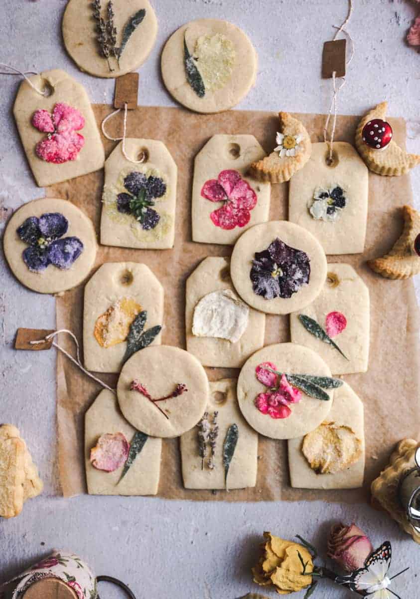 overhead shot of tea bag shaped sugar cookies on parchment paper with gorgeous colorful edible flowers on top