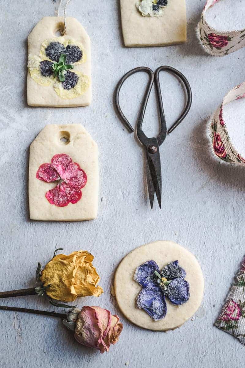 overhead close up image of sugar cookie shaped like circles and tea bag with flowers and a pair of garden scissors next to them