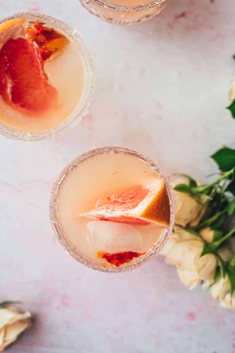 overhead shot of glass of grapefruit juice cocktail with cream roses next to it