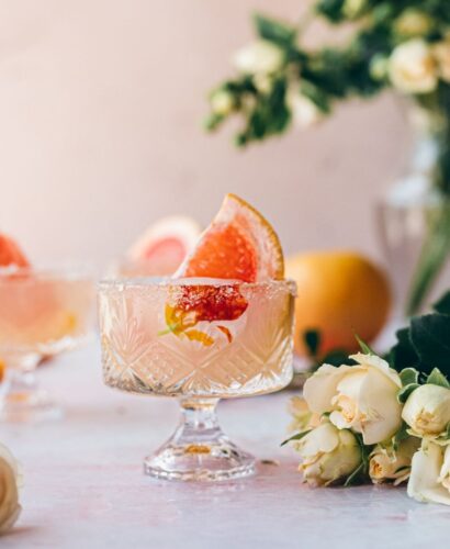image of small Dublin glass with a large grapefruit garnish and surrounded by cream colored flowers