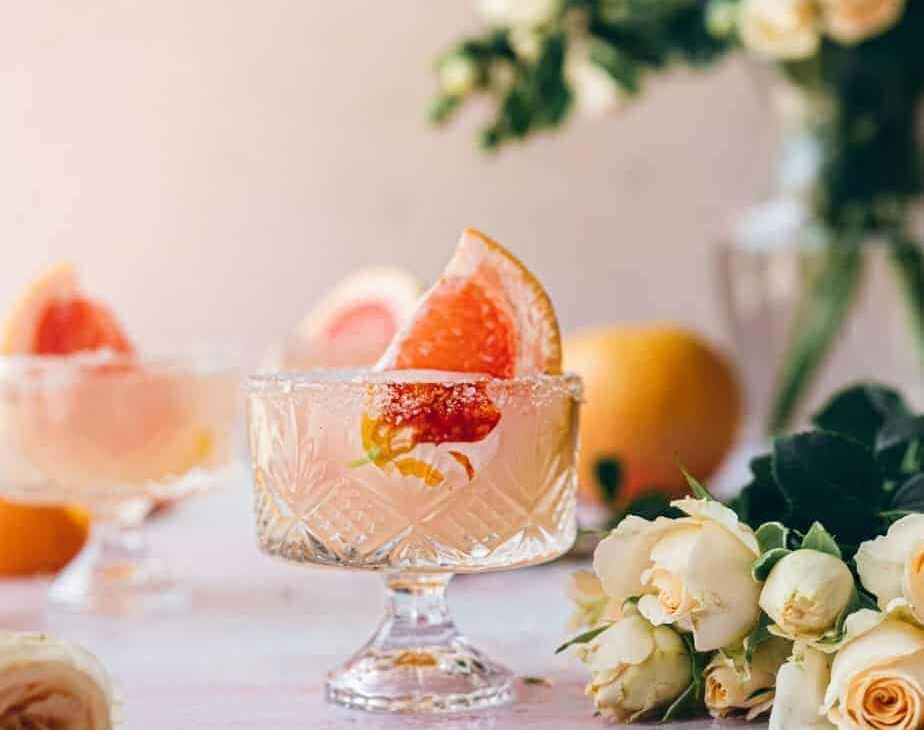 image of small Dublin glass with a large grapefruit garnish and surrounded by cream colored flowers