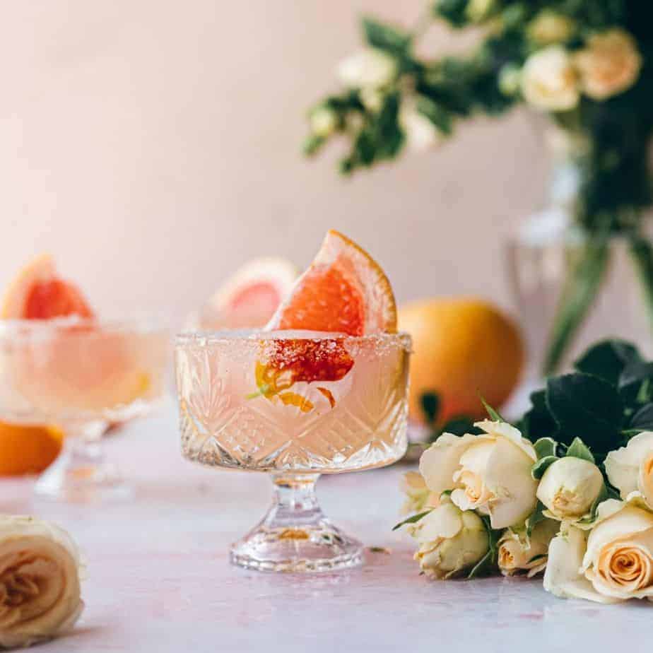 image of small Dublin glass with a large grapefruit garnish and surrounded by cream colored flowers