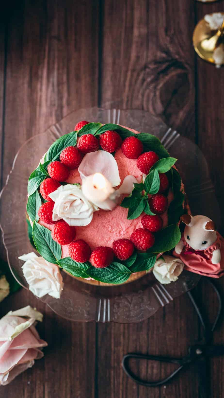 overhead shot of pink frosted cake garnished with raspberries in a circle and basil leaves