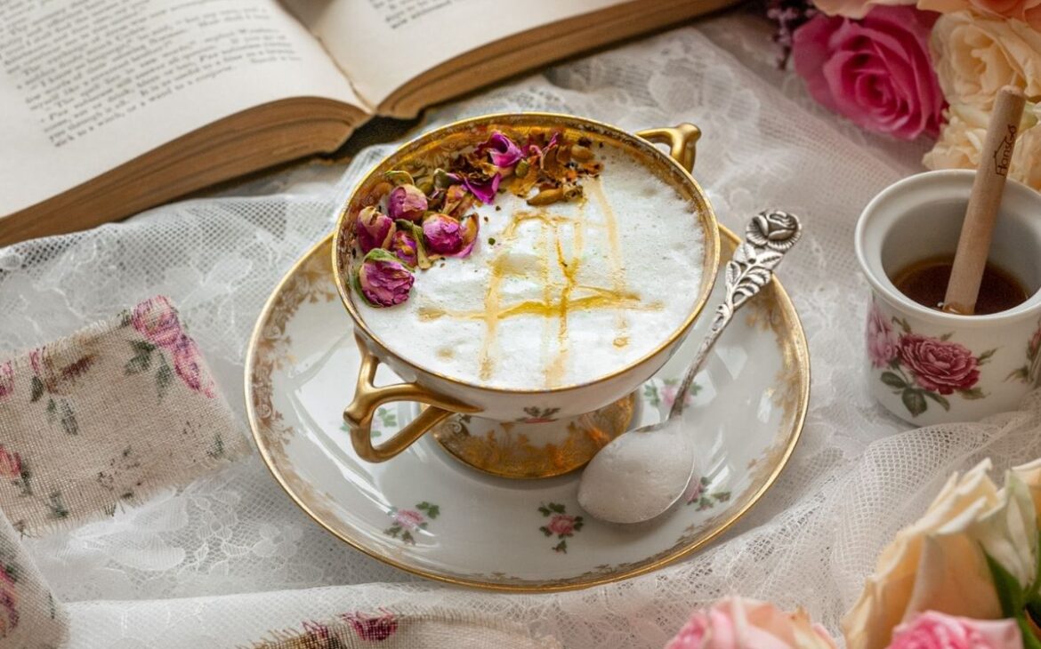 close up image of vintage tea cup filled with frothed milk topped with rose bud petals and honey