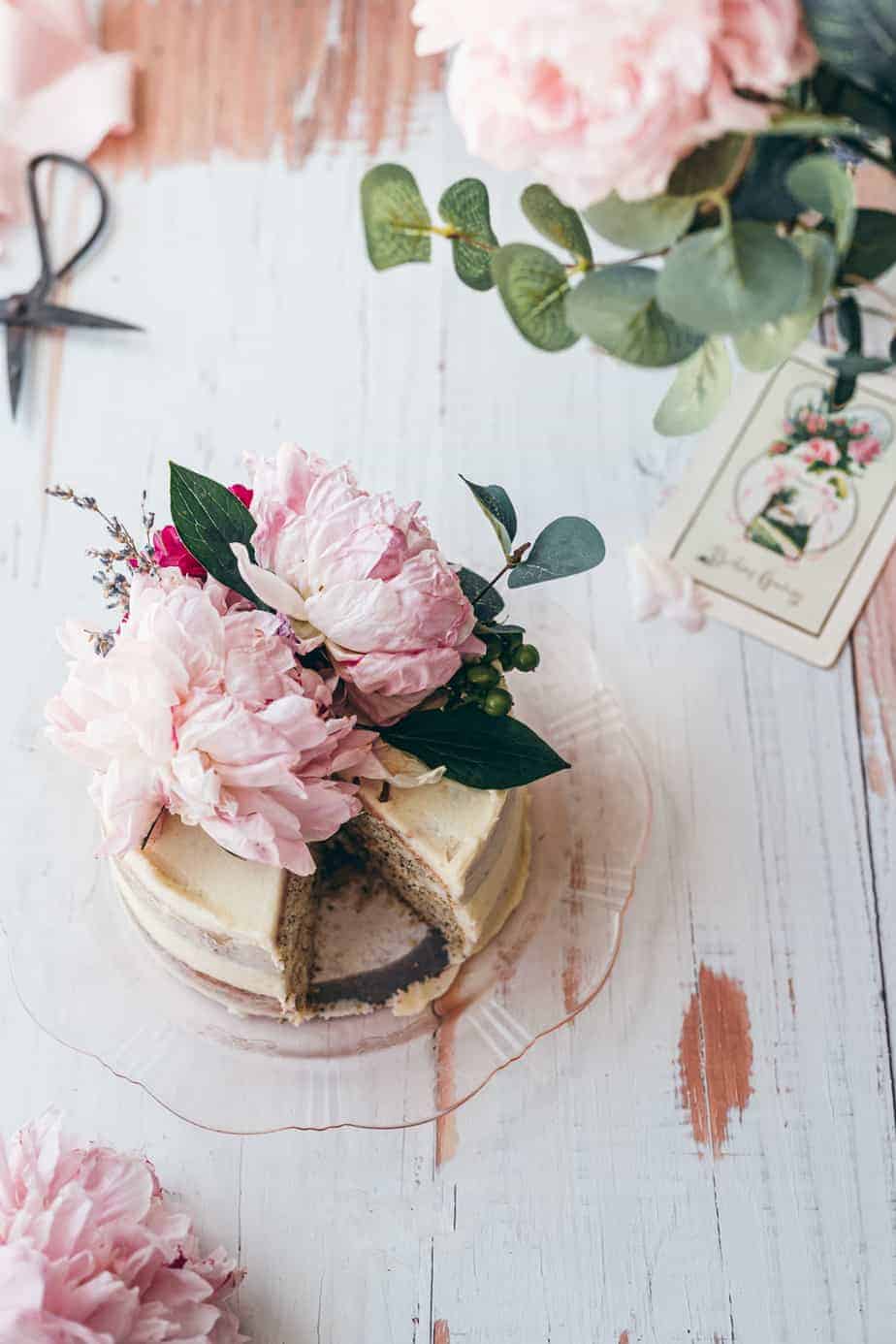 overhead shot of lavender earl grey cake on a white wooden rustic background topped with peonies flowers and eucalyptus 