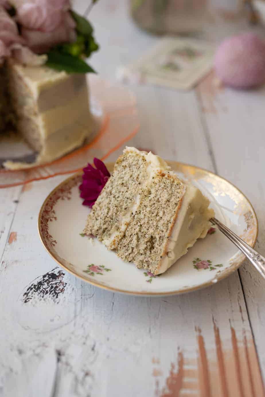 vintage plate with slice of frosted cake, showing two layers with buttercream in the center and a magenta flower on top on a white wooden rustic table