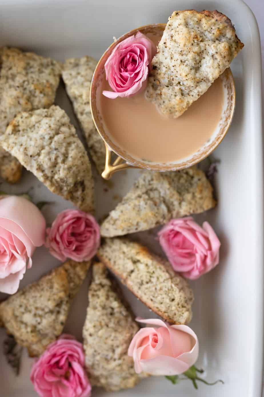 close up overhead image of vintage tea cup filled with earl grey tea with milk and a baking tin of scones and pink roses