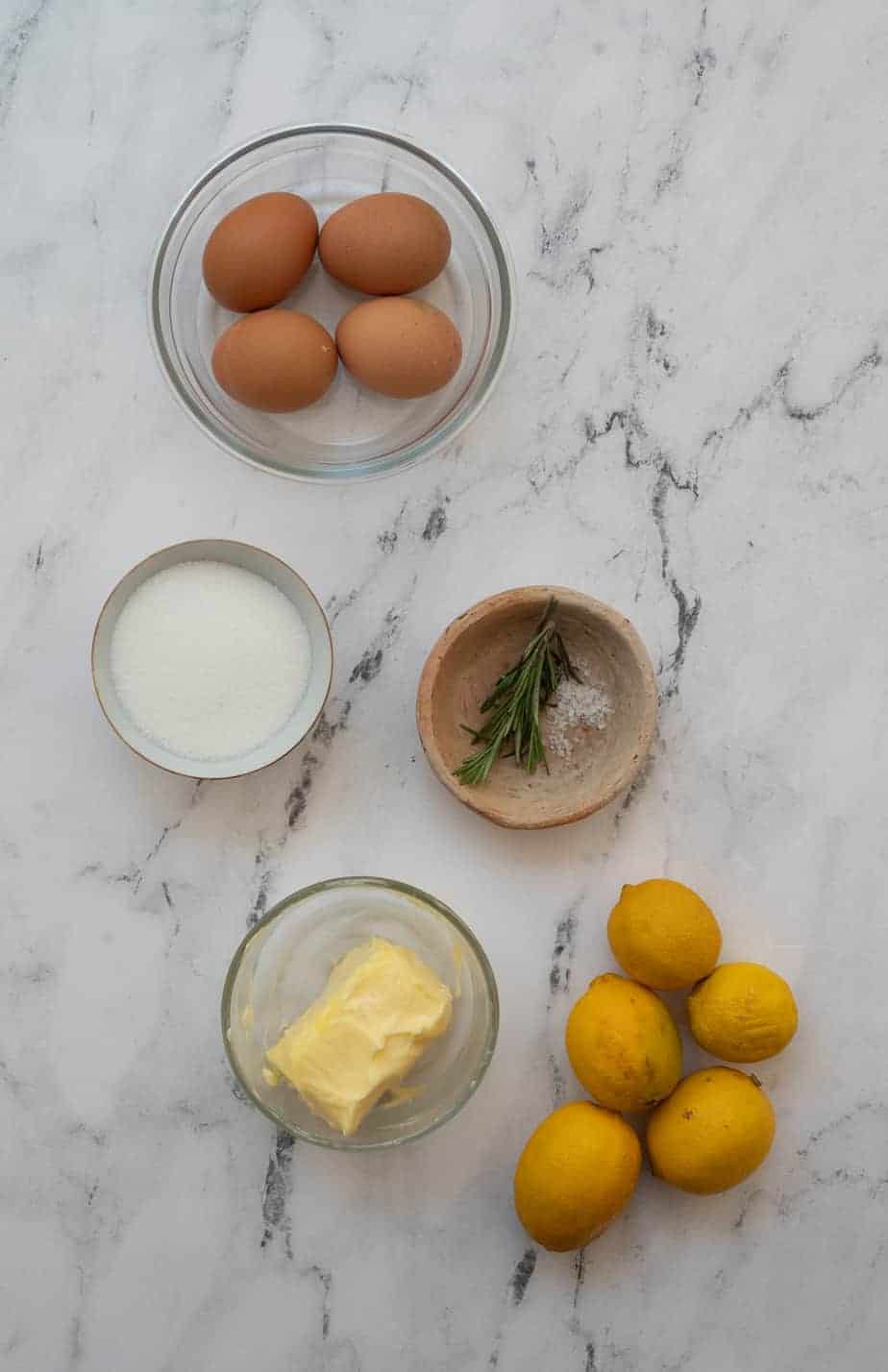 ingredients in rosemary lemon curd in small bowls on a bright marble background
