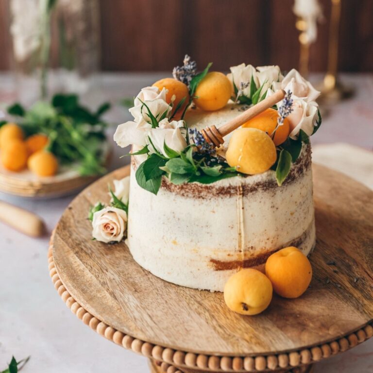 cover image of lavender apricot cake on wooden cake stand small white cake drizzled in honey with apricots on top and small roses
