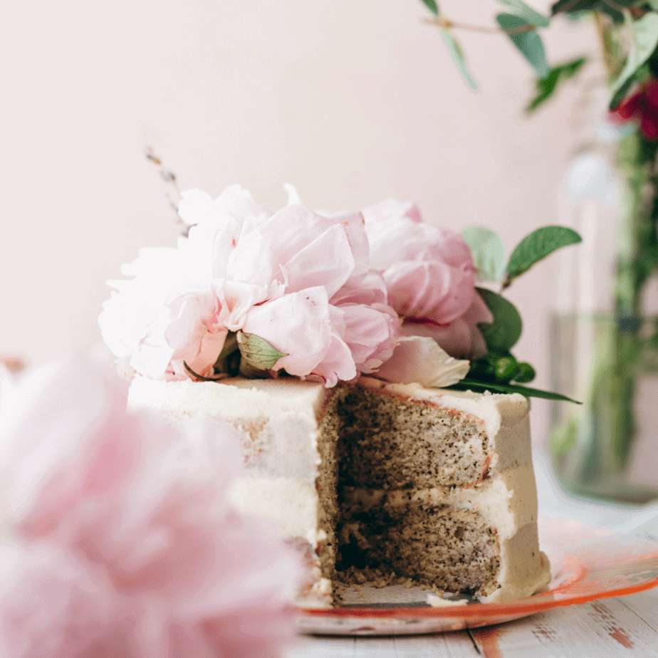 image of small layered cake with pink flower on top with vase with pink flowers in background