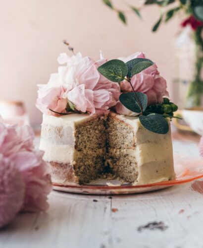 close up image of a small frosted cake sliced in the middle to show tea infused layers topped with pink peonies with a pink background