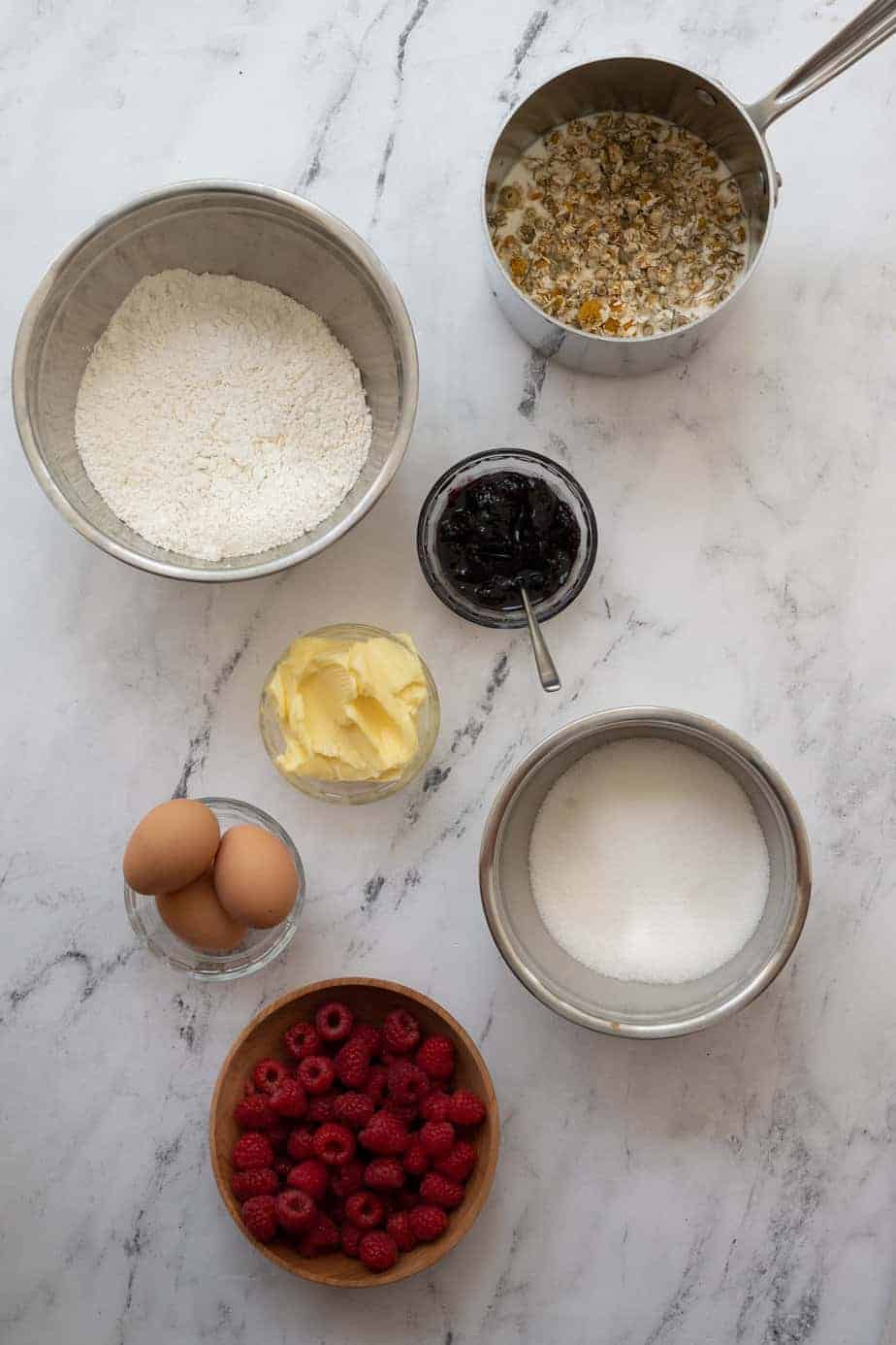 overhead flatly of bowls with ingredients for raspberry chamomile cake, flour, butter, eggs, sugar, chamomile cream