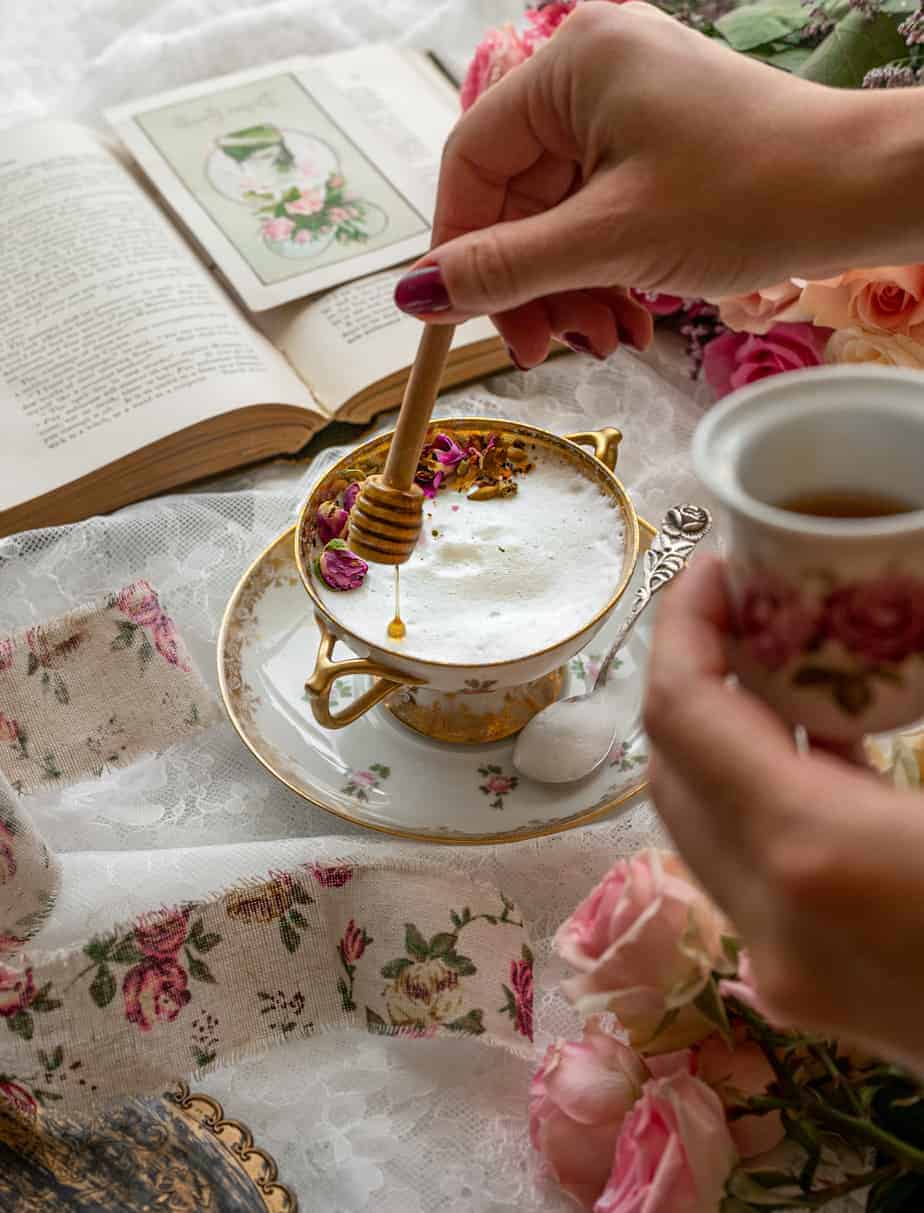 woman's hand drizzling honey with honey comb stick into vintage glass with frothed milk