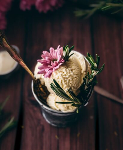 close up shot of rosemary ice cream in a small metal tin with fresh rosemary sprig and a flower