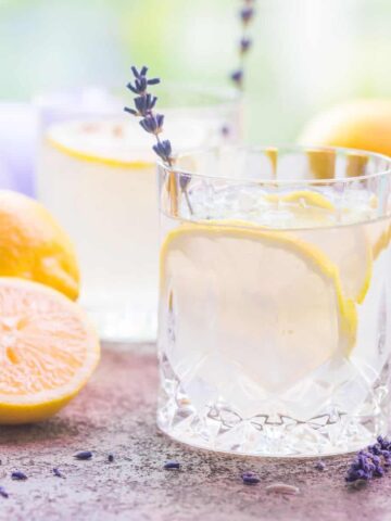 close up image of crystal glass filled with clear cocktail with a lavender sprig and lemon slice