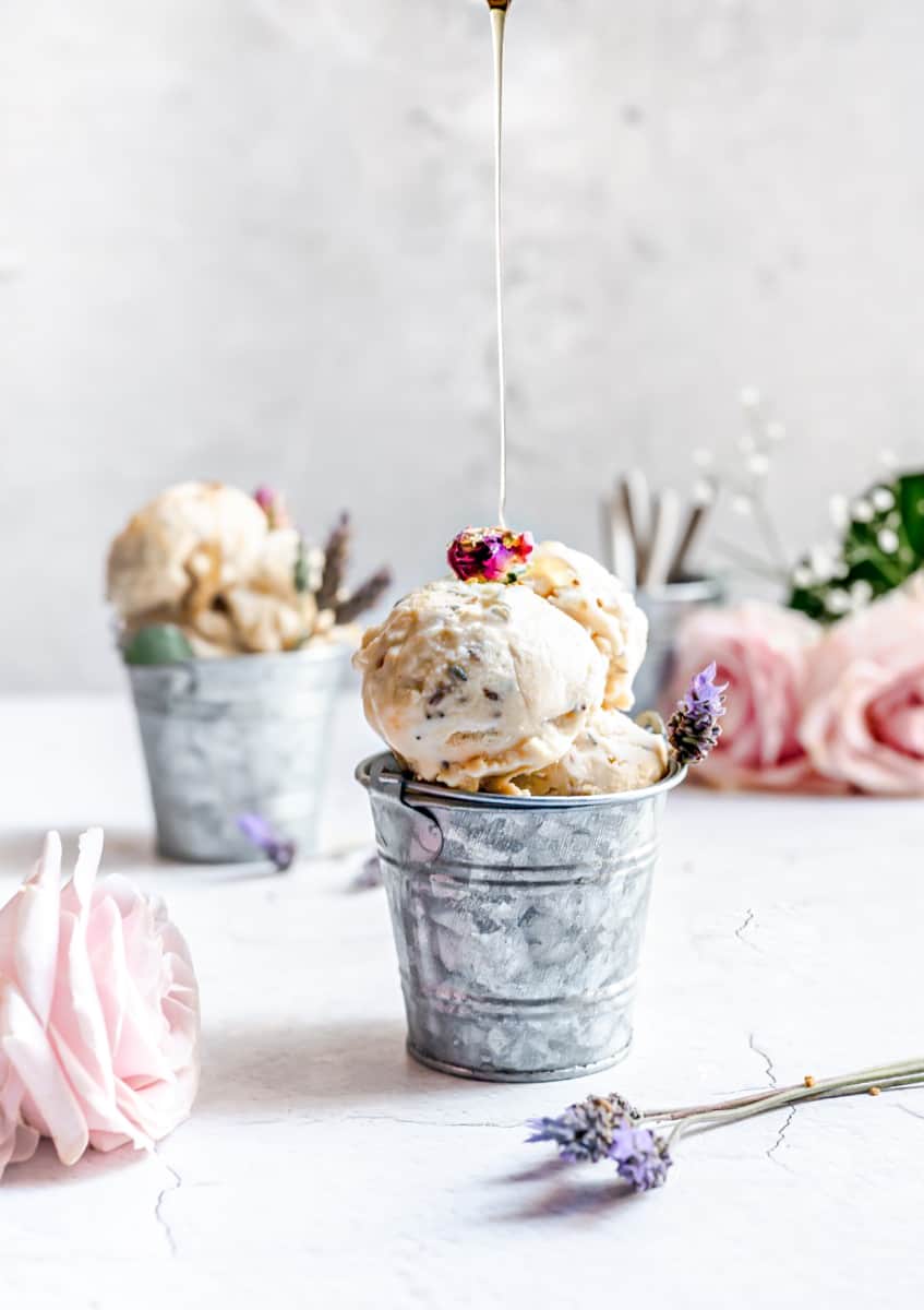 mini tin buckets filled with light colored scoops of lavender ice cream being drizzled with floral honey and surrounded by pink roses