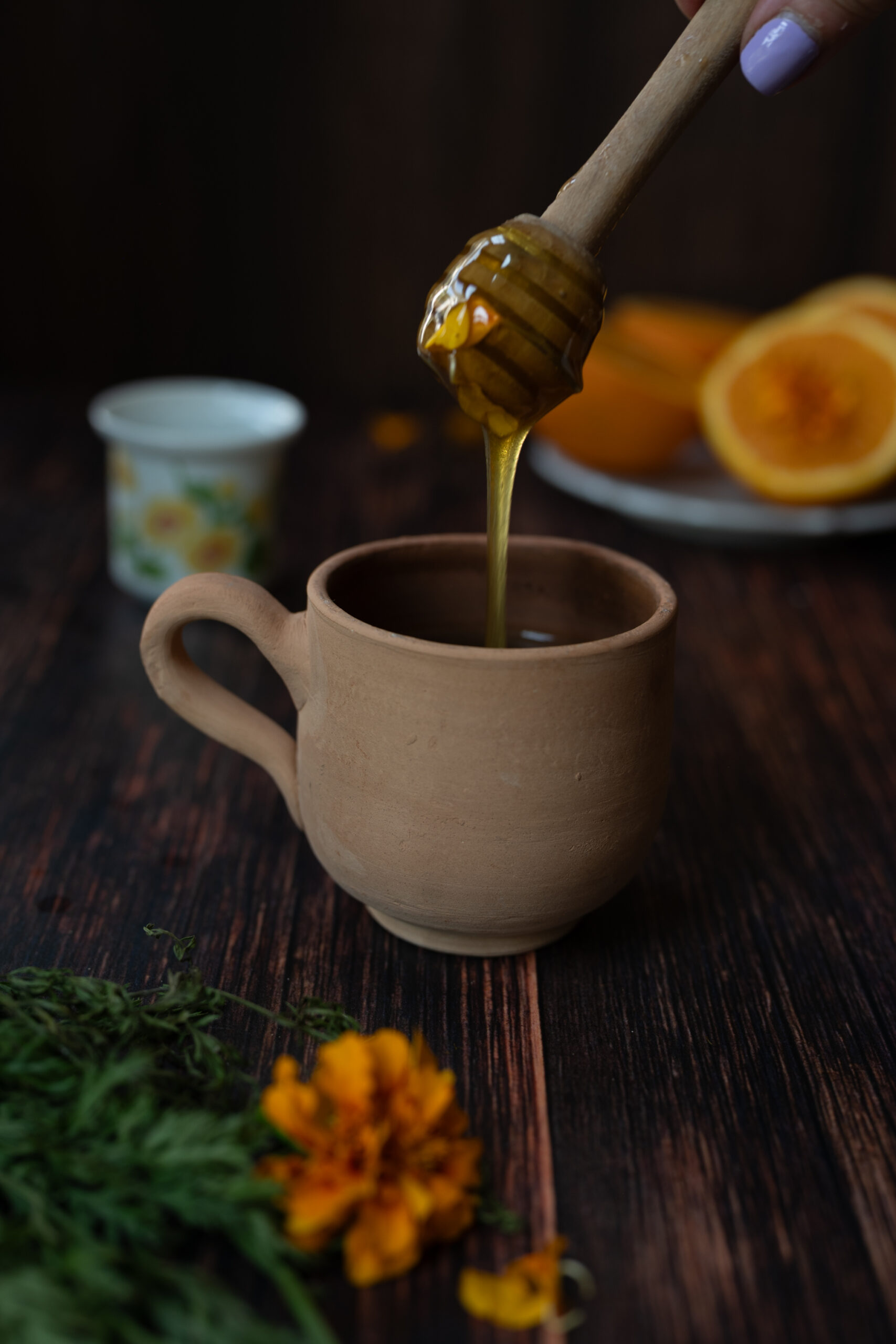 Honey drizzling into clay cup filled with marigold tea from fresh marigolds in garden