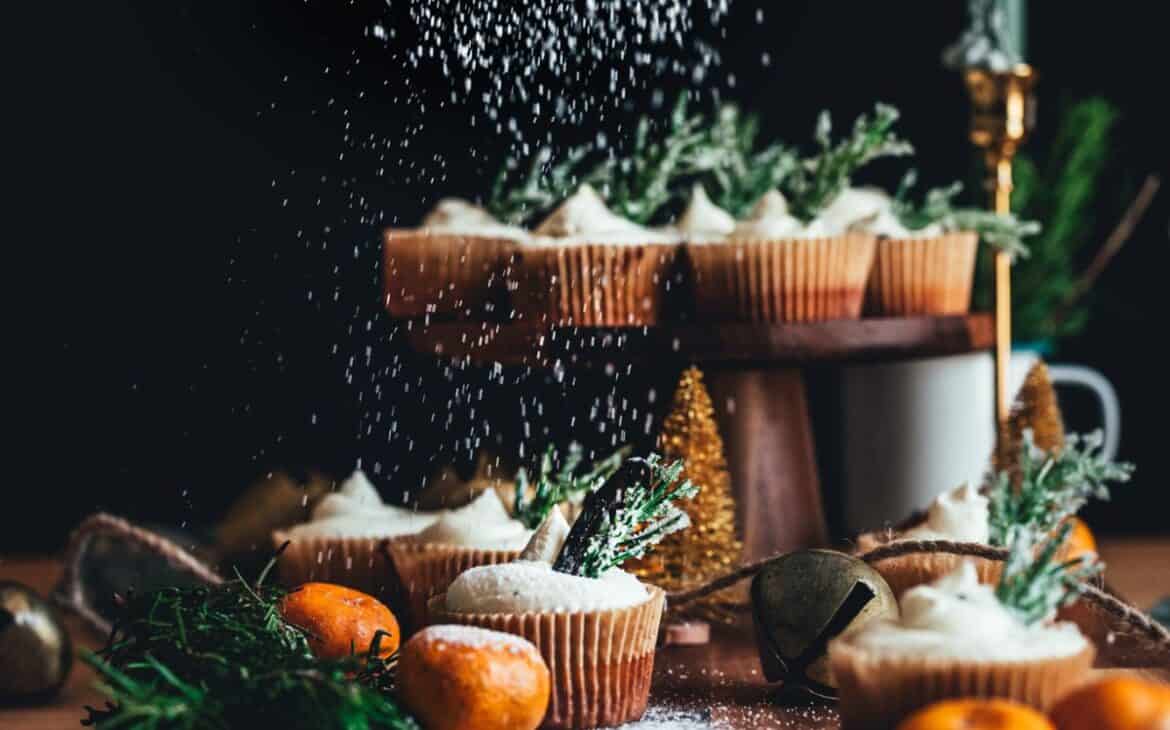 image of powdered sugar being sprinkled onto orange rosemary cupcakes with clementines and rosemary sprigs