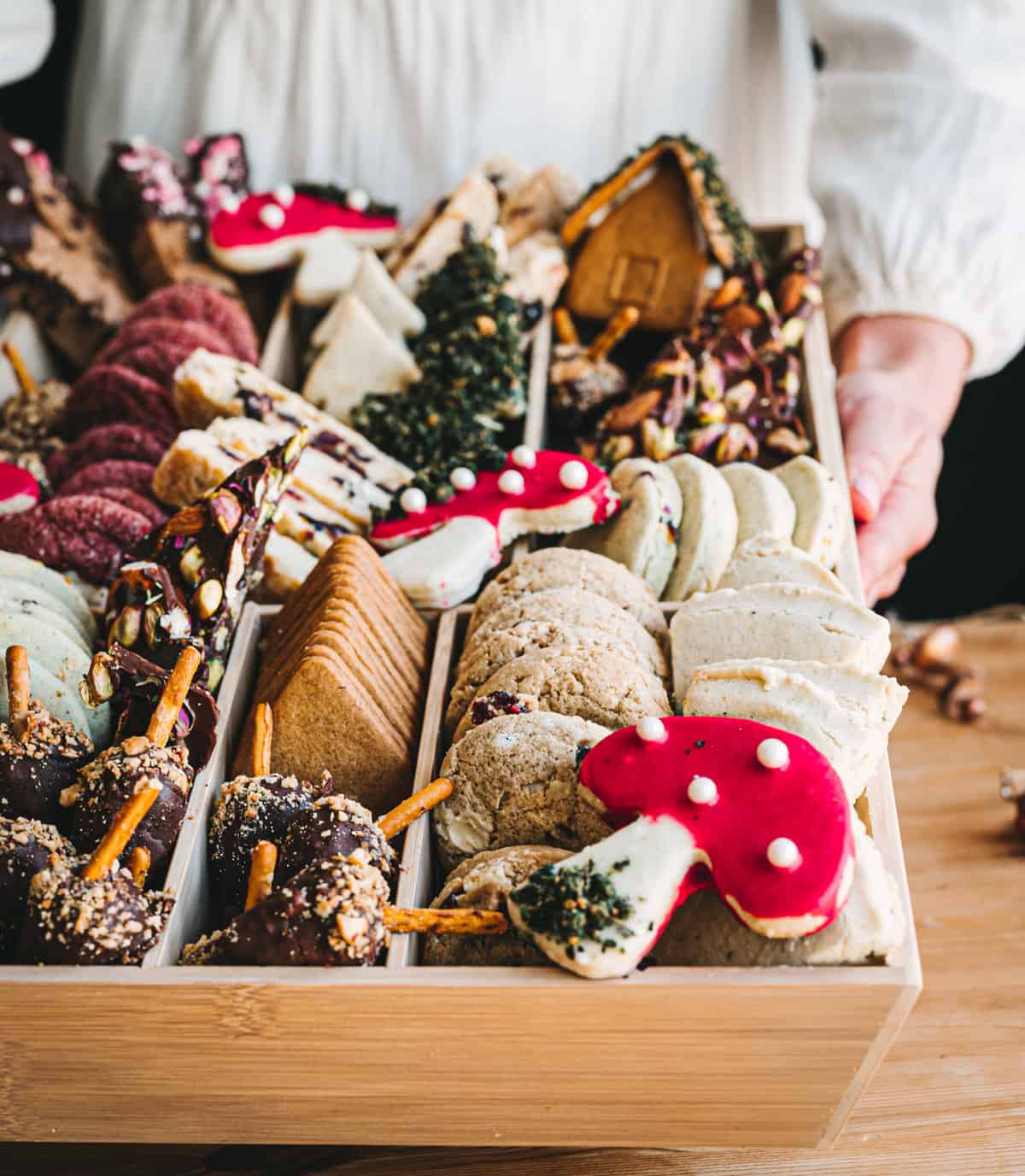 woman with white dress holding large box of cookies with woodland designs including acorn truffles