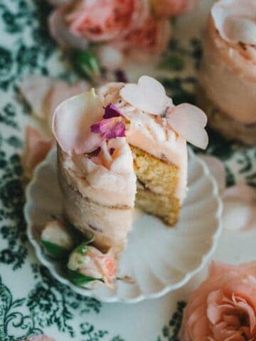 close up image of mini cake sliced with pink rose buttercream with a sugar butterfly, and soft pink rose petals on a mini scalloped plate