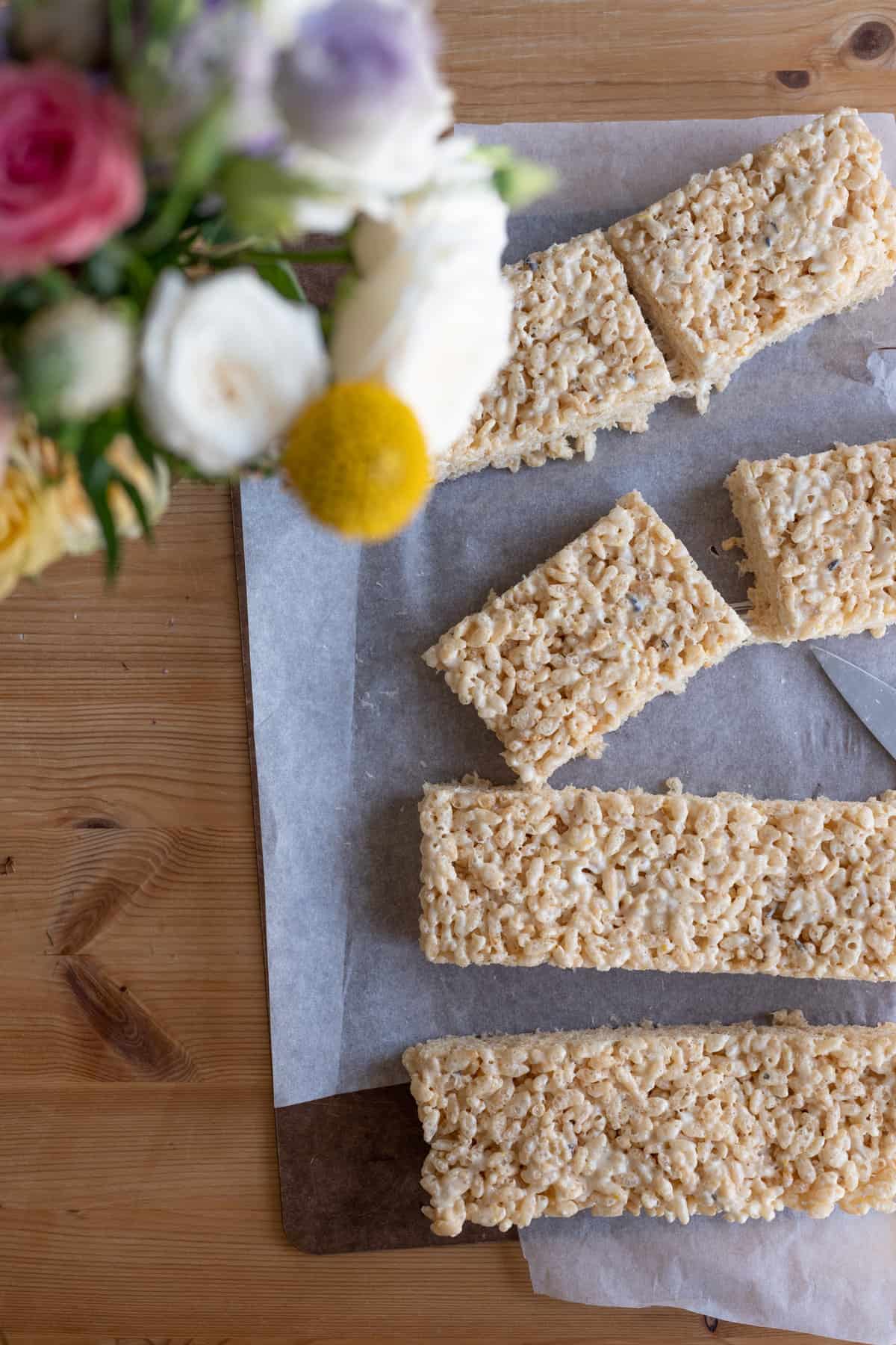 overhead image of rice krispy treats on white wax paper on a rustic table top sliced into rectangles and placed on an angle