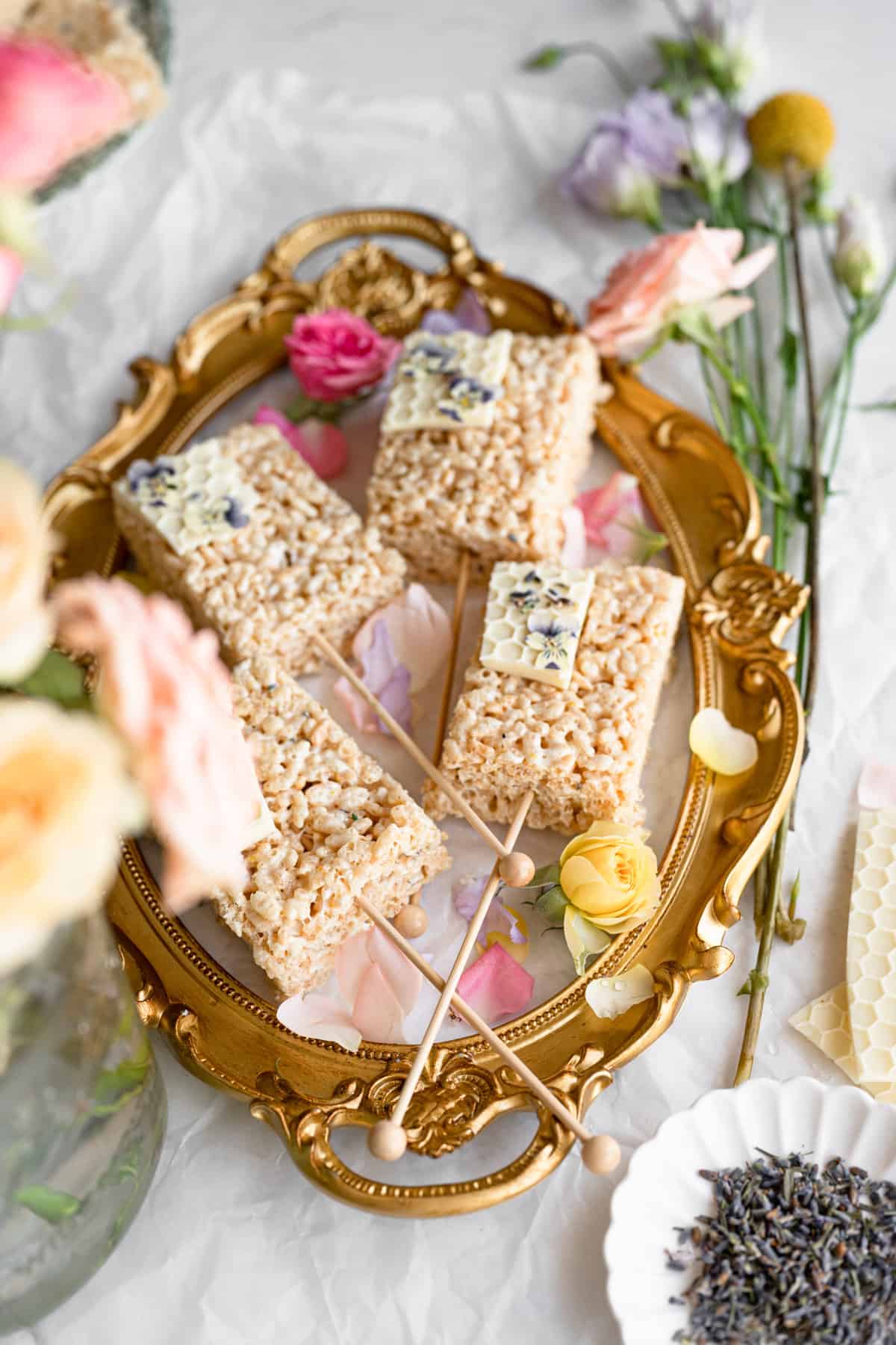 angled image of lavender lemon rice krispy treats topped with white chocolate honey comb, surrounded by pastel flower petals