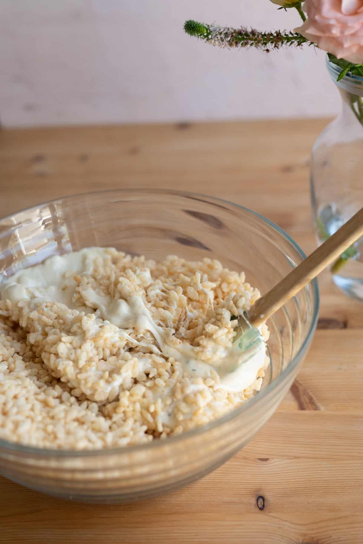 glass bowl filled with rice krispy treats and melted marshmallows with a small spatula sticking out of it on a wooden rustic table