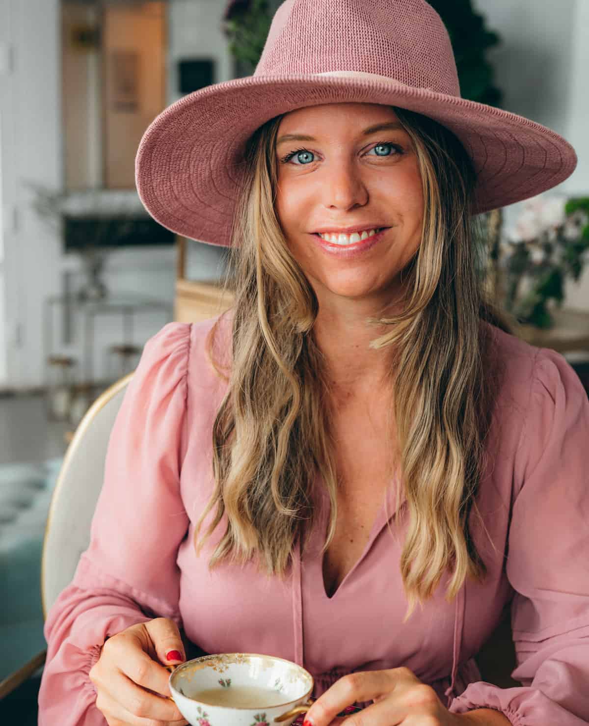 warm photo of woman with honey brown hair smiling with pink hat and pink Dress with bright blue eyes