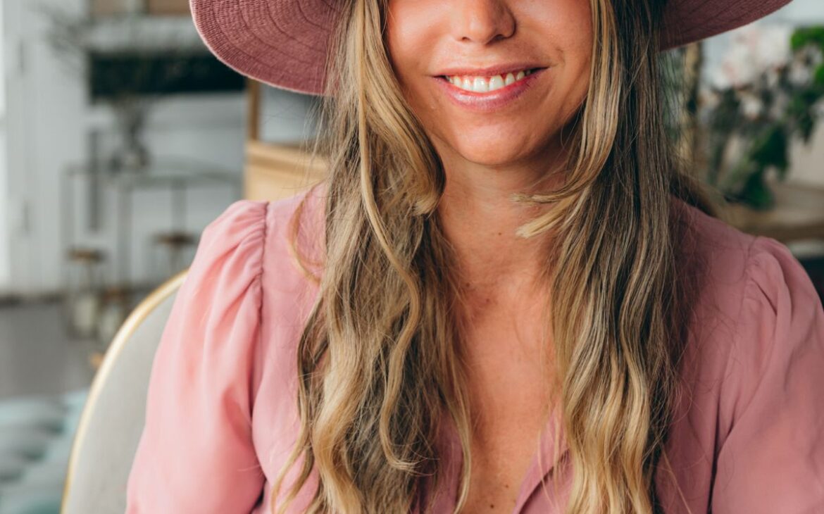 warm photo of woman with honey brown hair smiling with pink hat and pink Dress with bright blue eyes