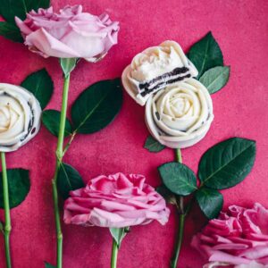 white chocolate covered oreo roses on vibrant pink surface surrounded by pink roses and stems