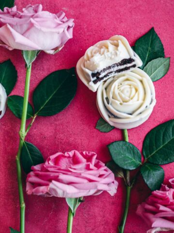 white chocolate covered oreo roses on vibrant pink surface surrounded by pink roses and stems