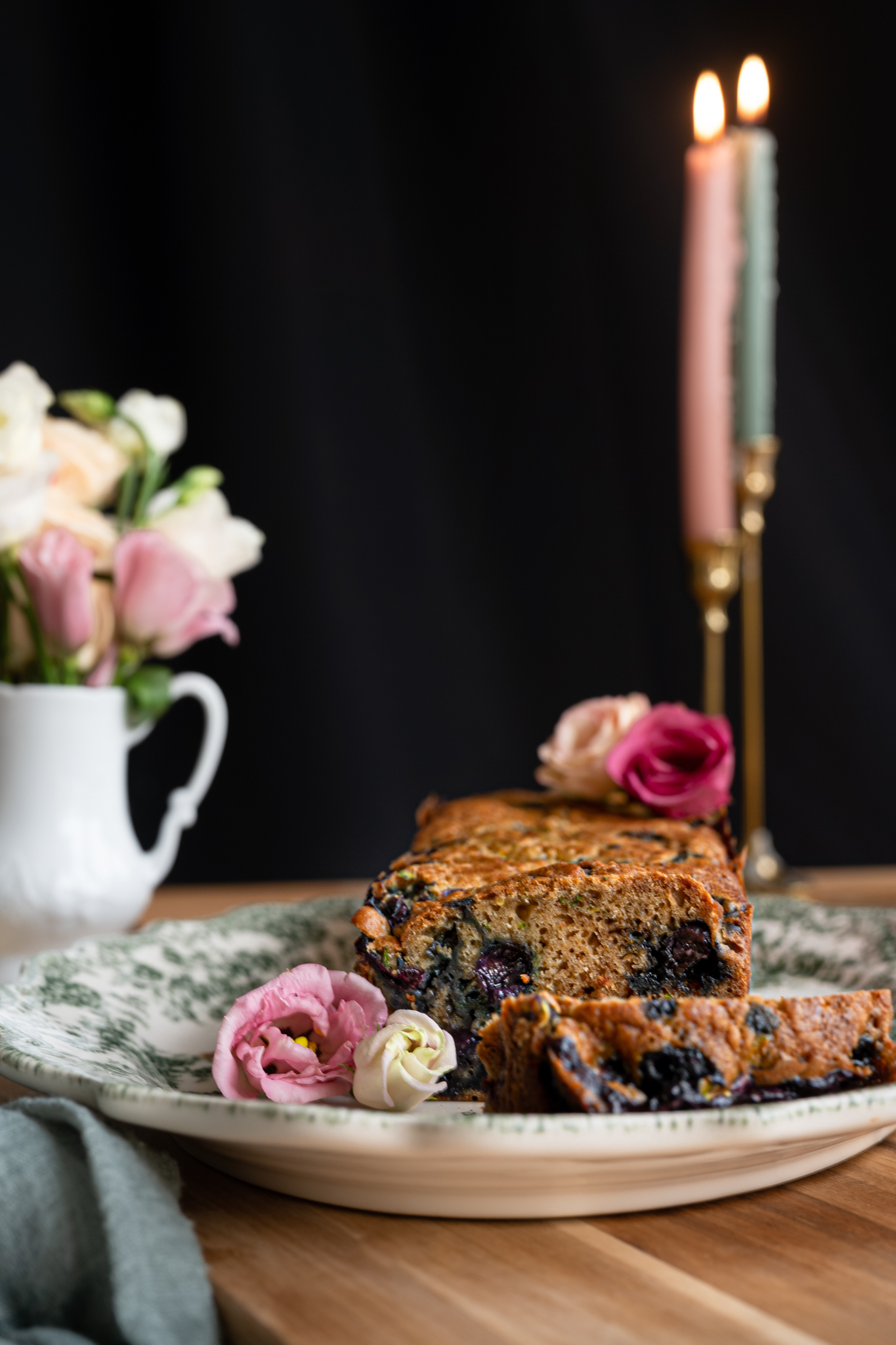 image of close up zucchini bread sliced into exposing blueberries in rustic still life scene with candles and flowers in the background