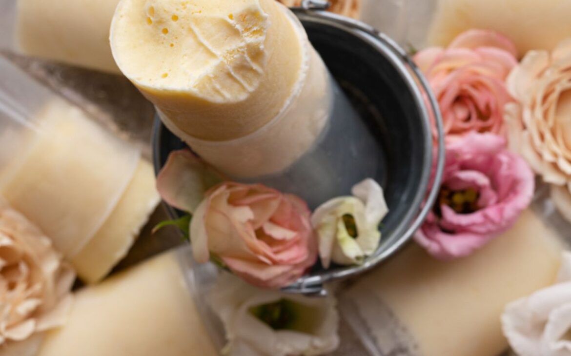 overhead shot looking directly down onto a creamy mango push pop with bite out of it surrounded by pretty pink and peach colored flowers