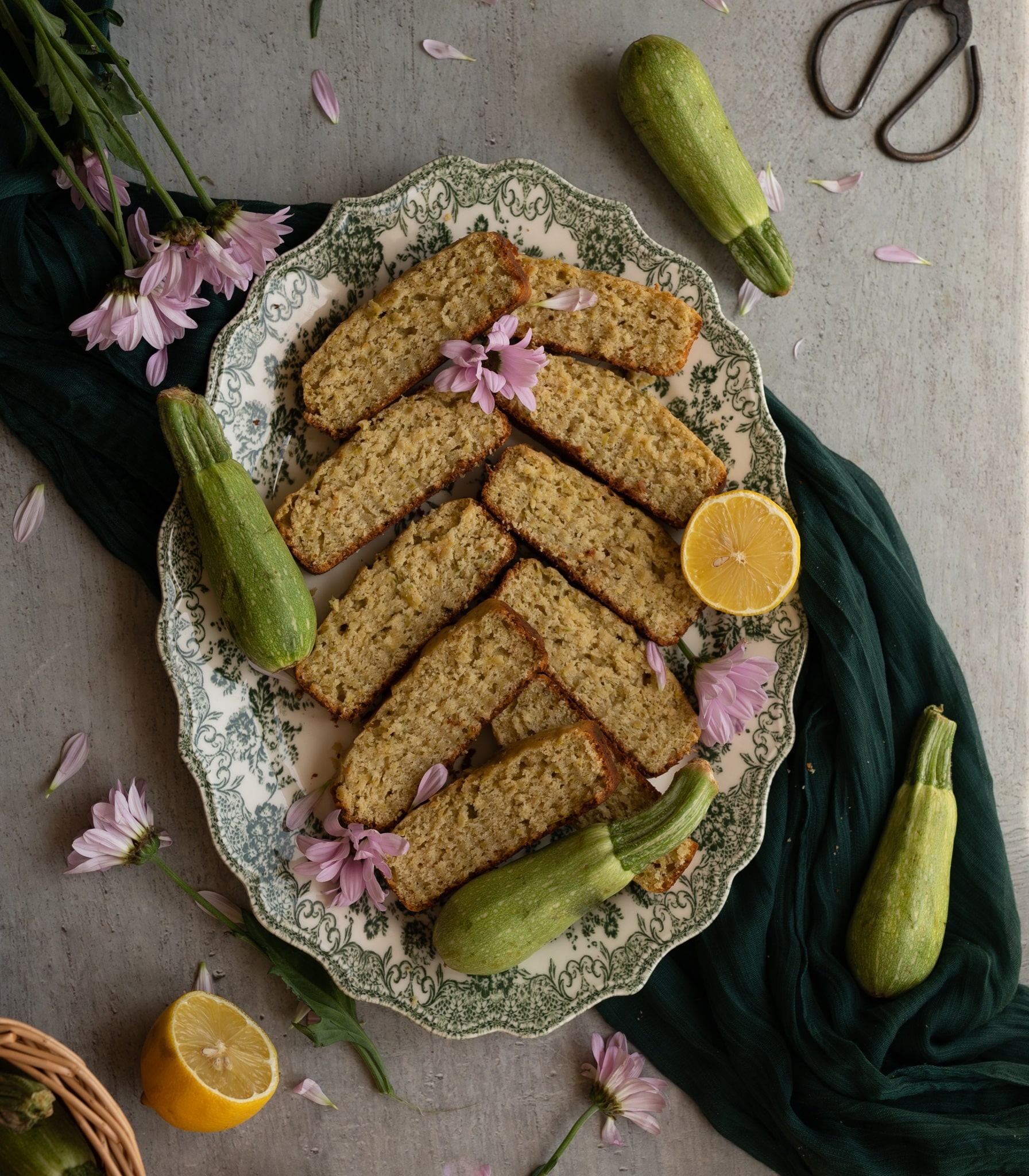 overhead image sliced lemon basil zucchini bread surrounded by zucchini and purple flowers