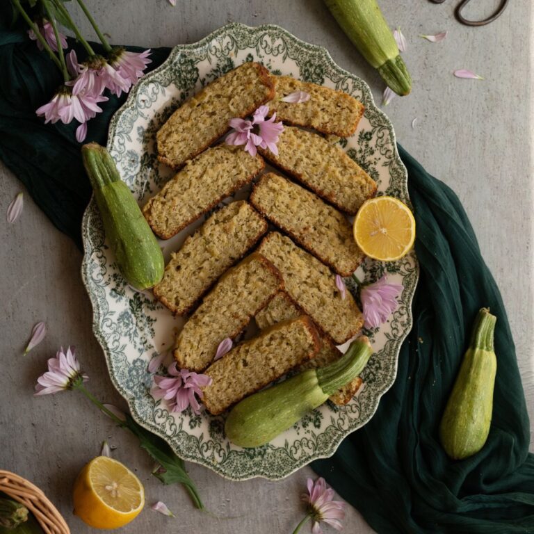 overhead image sliced lemon basil zucchini bread surrounded by zucchini and purple flowers