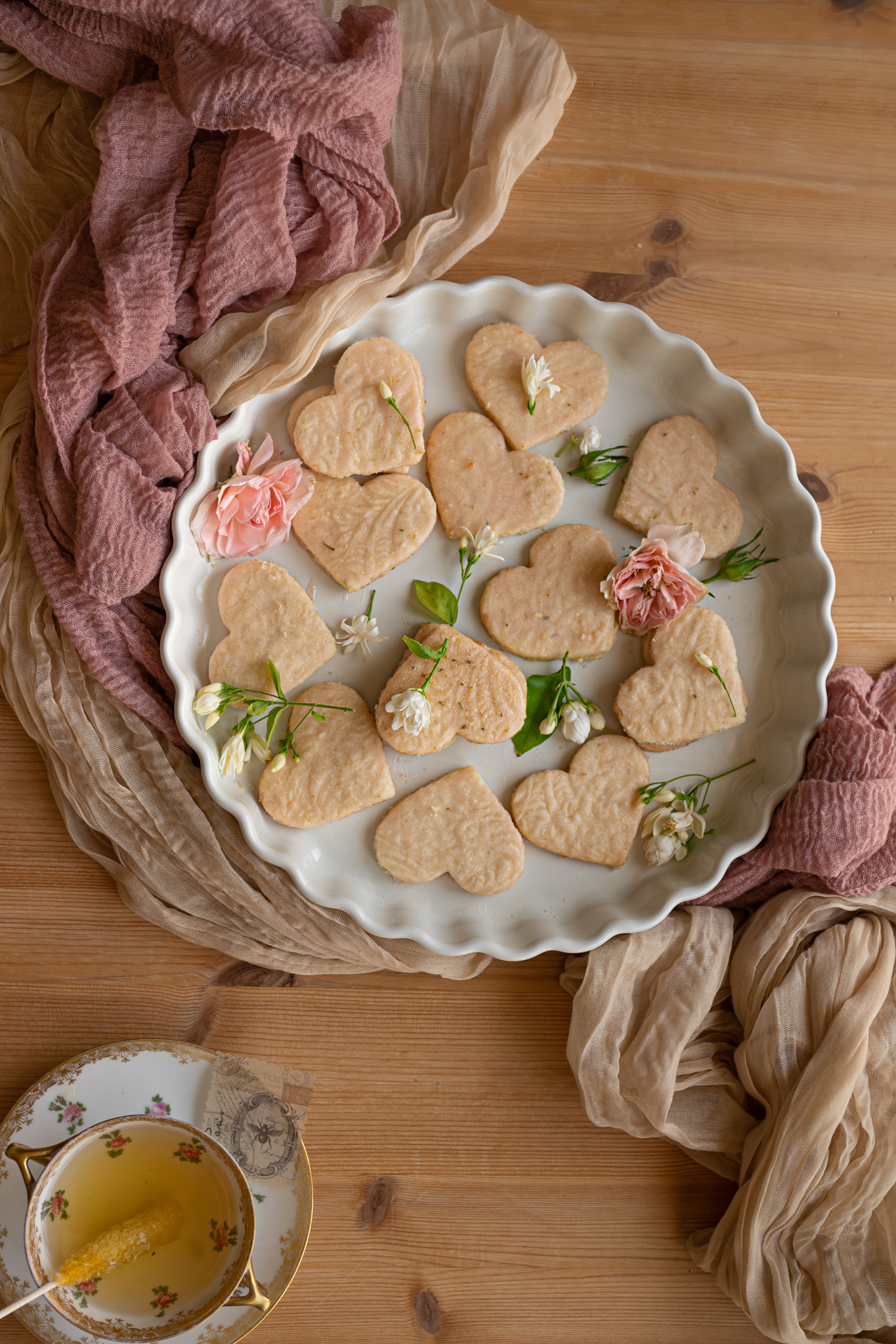 overhead image of jasmine tea shortbread heart shapped with pink rose and fresh jasmine on white scalloped dish