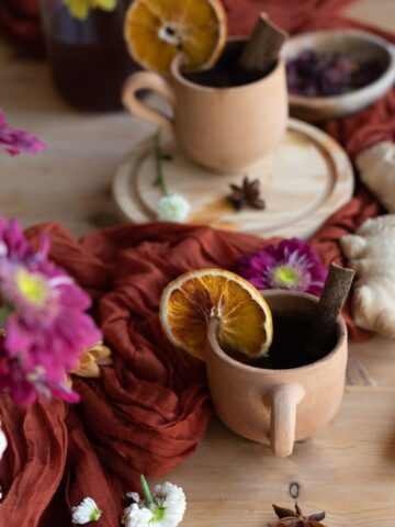 close up image of terracotta cup with orange slice and big piece of ginger showing healing herbal spiced cider