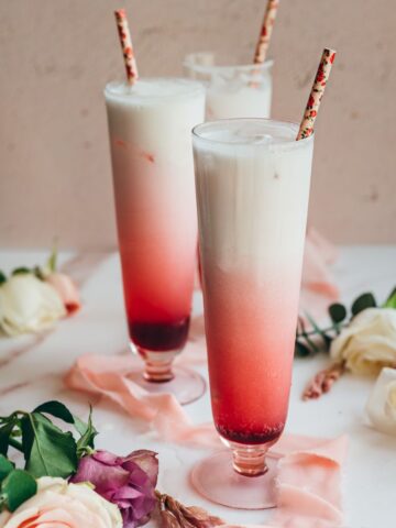 close up image of three tall glasses filled with hibiscus syrup, sparkling water and cream for hibiscus italiann soda