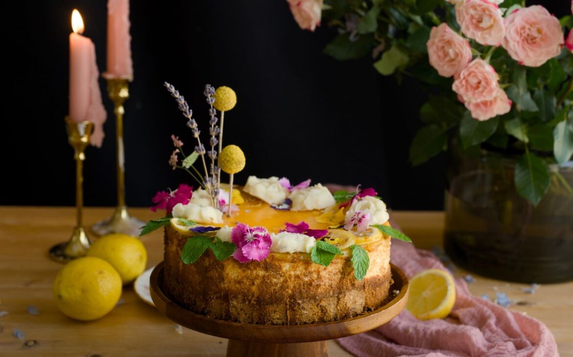 photo of lavender lemon cheesecake on wooden cake stand next to pink roses and in front of pink candles